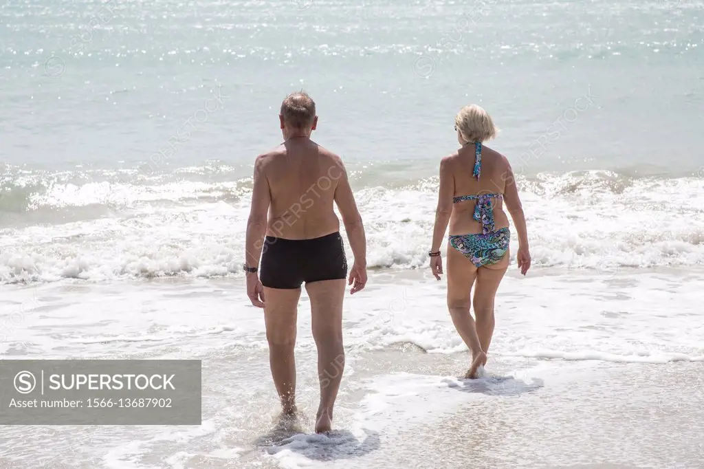 Older retired caucaisian couple going into the ocean at the beach in the tropical island of Martinique.