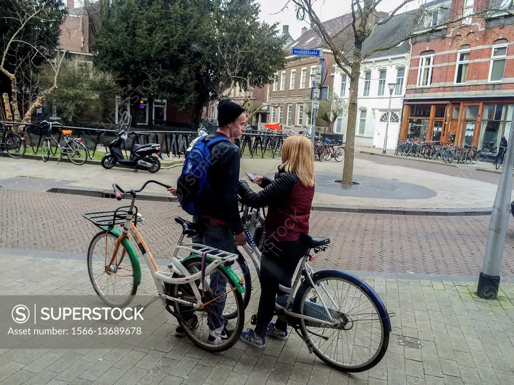 Tilburg, Netherlands. Young male and female couple, holding their bikes, meeting in the streets of Tilburg.