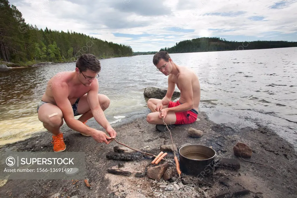 Brothers grilling hot dogs by the water, countryside of northern Sweden.
