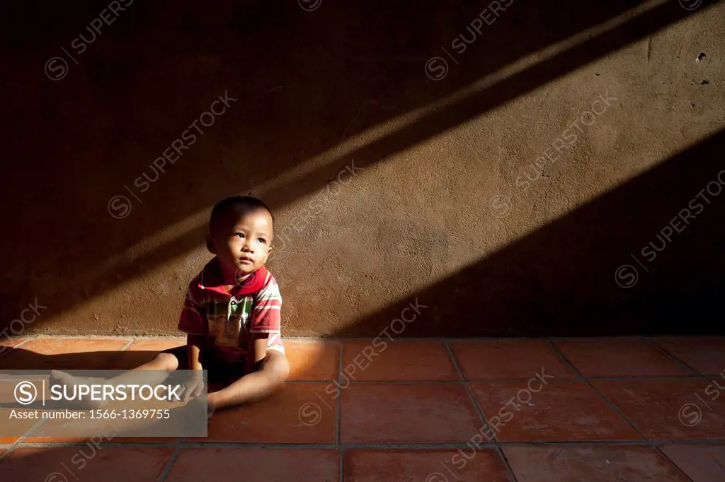 A toddler sits in a shaft of light in a village outside of Phnom Penh, Cambodia.