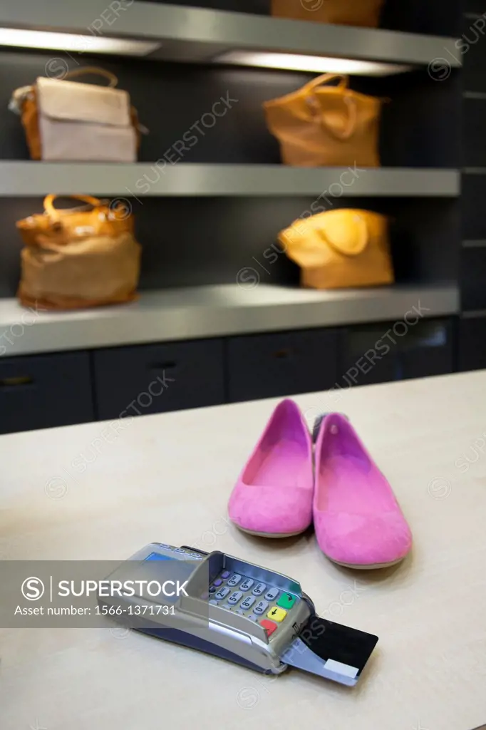 Shoes on clerk desk in retail shop. Card reader and bags or shoulder bags. Pricing, debit machine, counter.