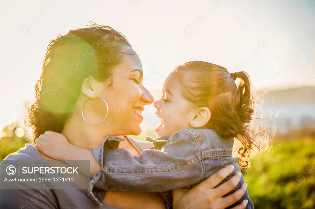 Mother and daughter embracing with the sun behind them.