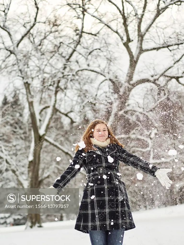 Beautiful young girl wearing a winter coat and throwing snow up in the air, Finnish winter day on February.