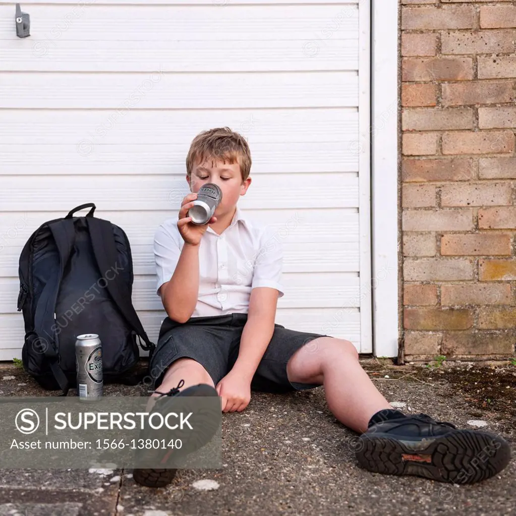 A boy of 10 in his school uniform drinking lager alcohol showing the affect of underage drinking in the Uk.