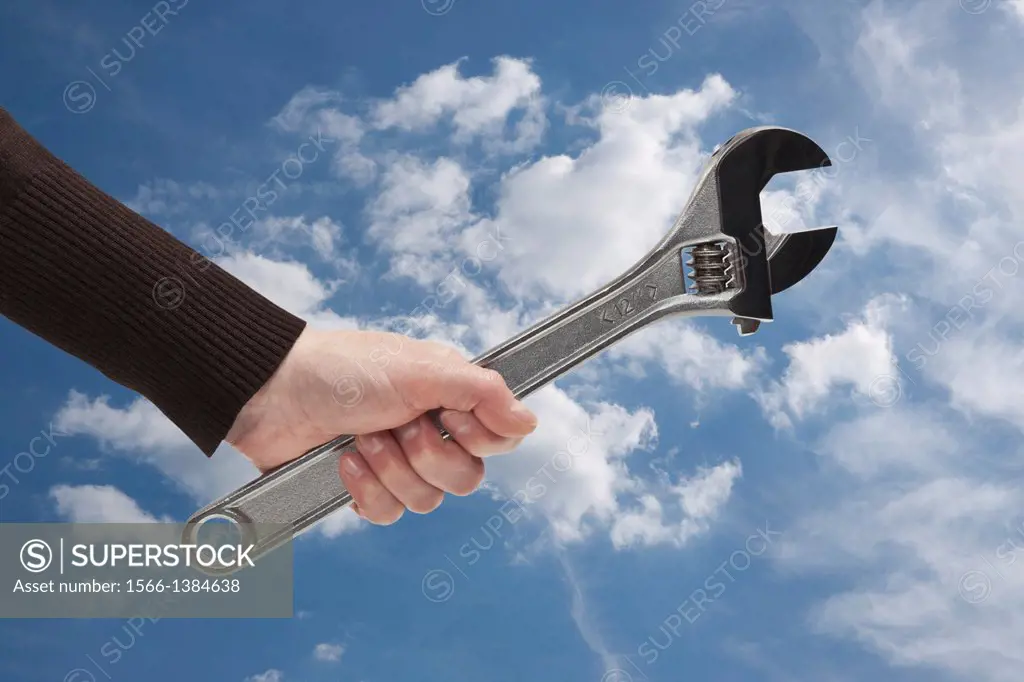 A adjustable spanner is hand-held, background sky and clouds.