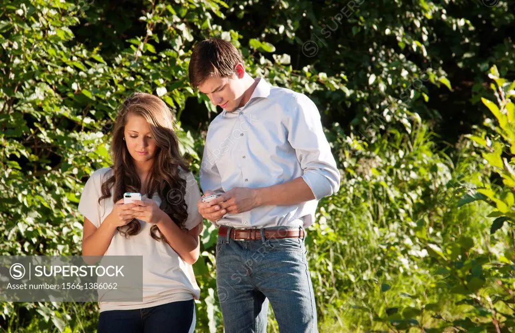 Young teenagers dating boy and girl aged 17 texting on Iphone together at home outdoors.