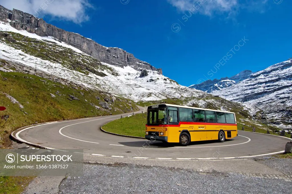 Yellow Swiss Post Bus bus in a hairpin bend on the mountain road to the pass Klausenpass against the peaks of the Glarus Alps near Urnerboden, Canton ...