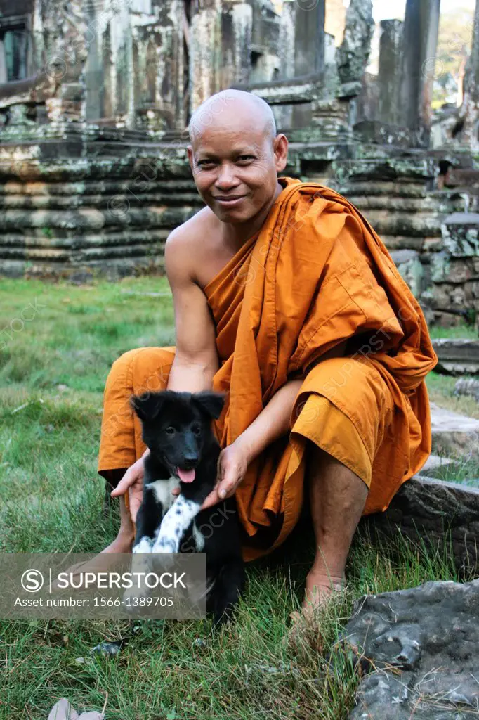 Buddhist monk playing with his dog on the grounds of Bayon, Angkor Thom.