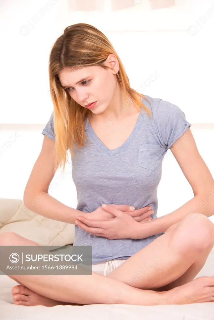 Young beautiful woman sitting on a bed and holding her stomach for pain