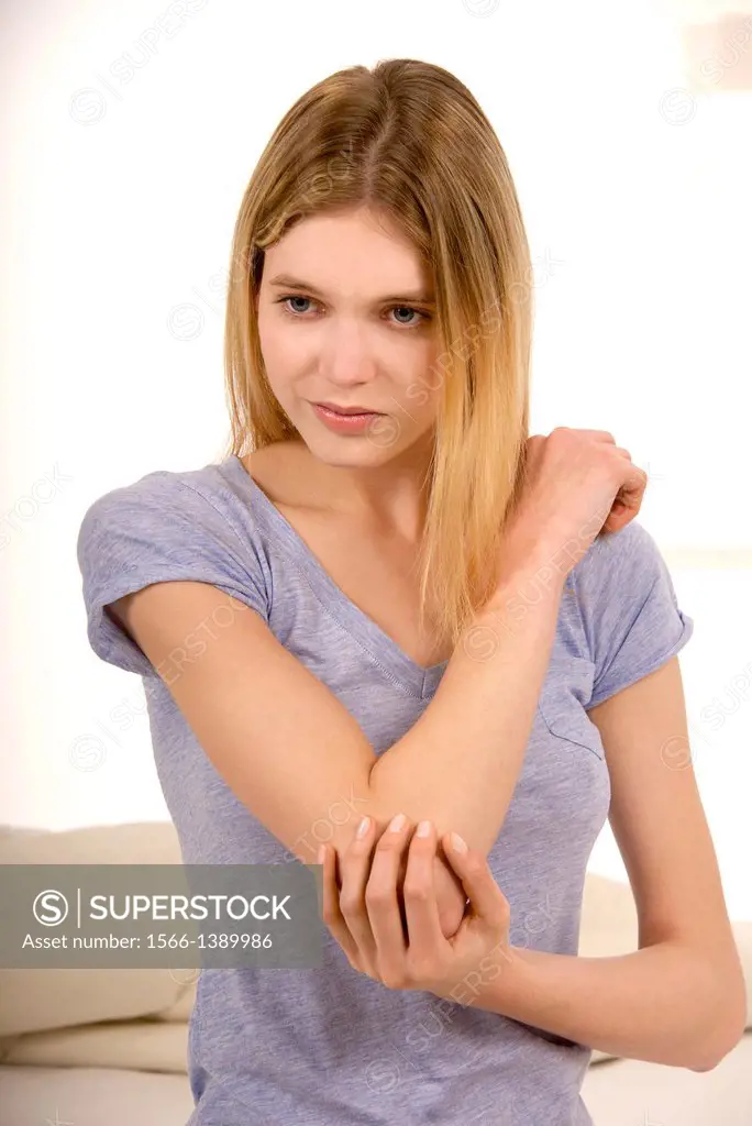 Young beautiful woman sitting on a bed and holding her stiff painful elbow