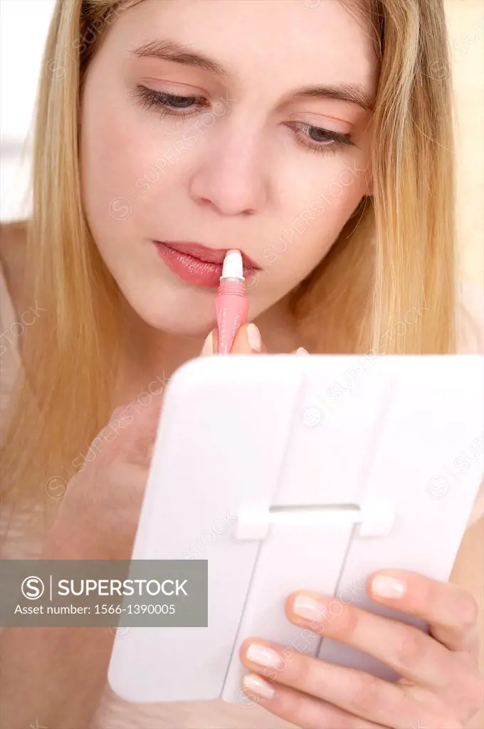 young woman making up and putting on lipstick or gloss