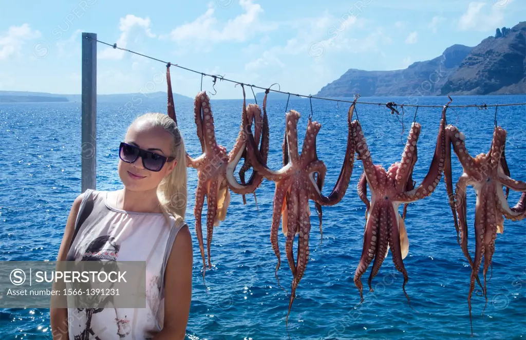 Greece Santorini Oia Cyclades Greek Islands fishing village with Europen woman tourist below Oia with octapus squid hanging on rope Greek; Islands; be...