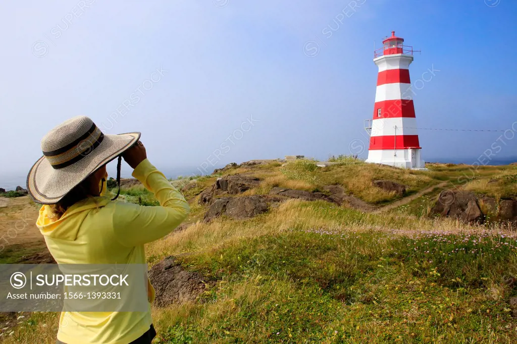 A woman looking through binoculars near the Brier Island Lighthouse at West Point, Brier Island, Nova Scotia, Canada