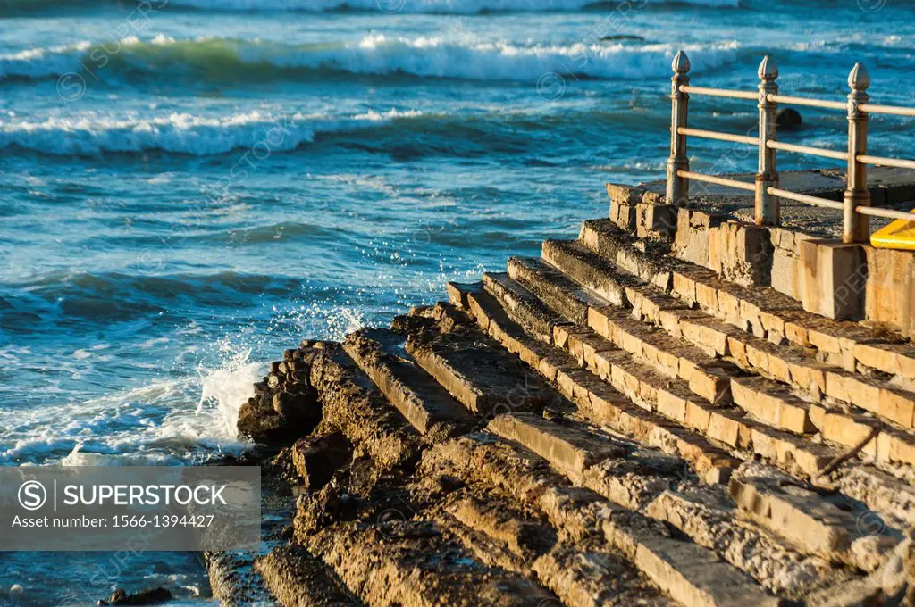 A battered seawall and steps, with rusted railings after many years of exposure to the elements. Cape Town, South Africa