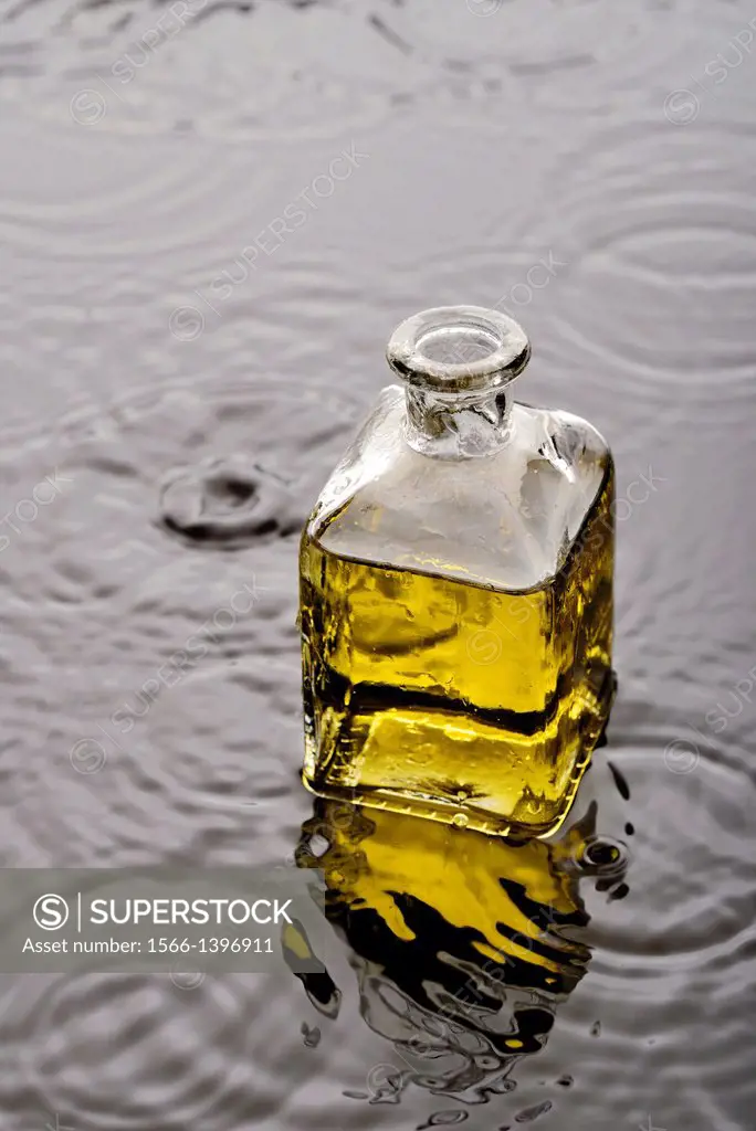 Líquido amarillo, aceite o perfume, en un frasco de vidrio sobre el agua con gotas de agua y ondas.