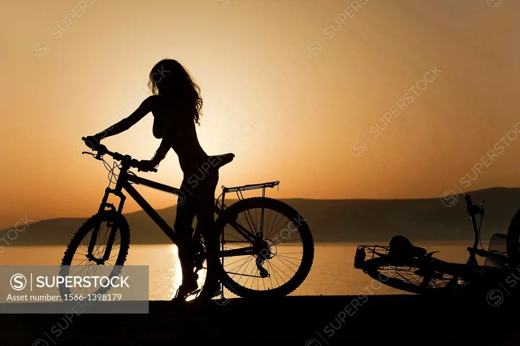 Woman with a bicycle near the sea at sunset, Koufonissi, Cyclades Islands, Greek Islands, Greece, Europe.