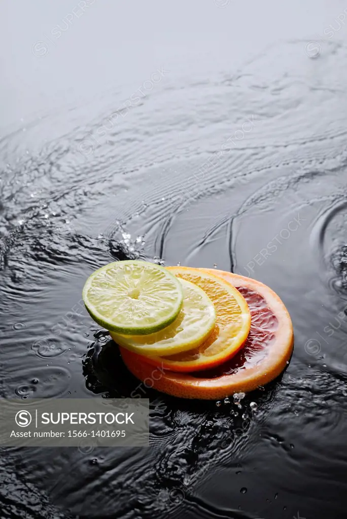 Citrus fruits, grapefruit, orange, lemon and lime slices splashing in water on black background.