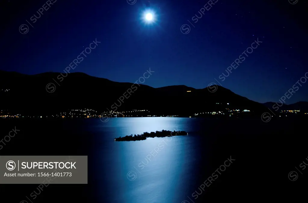 Moon light reflected over an alpine lake maggiore with brissago islands and mountains at night in ticino switzerland.