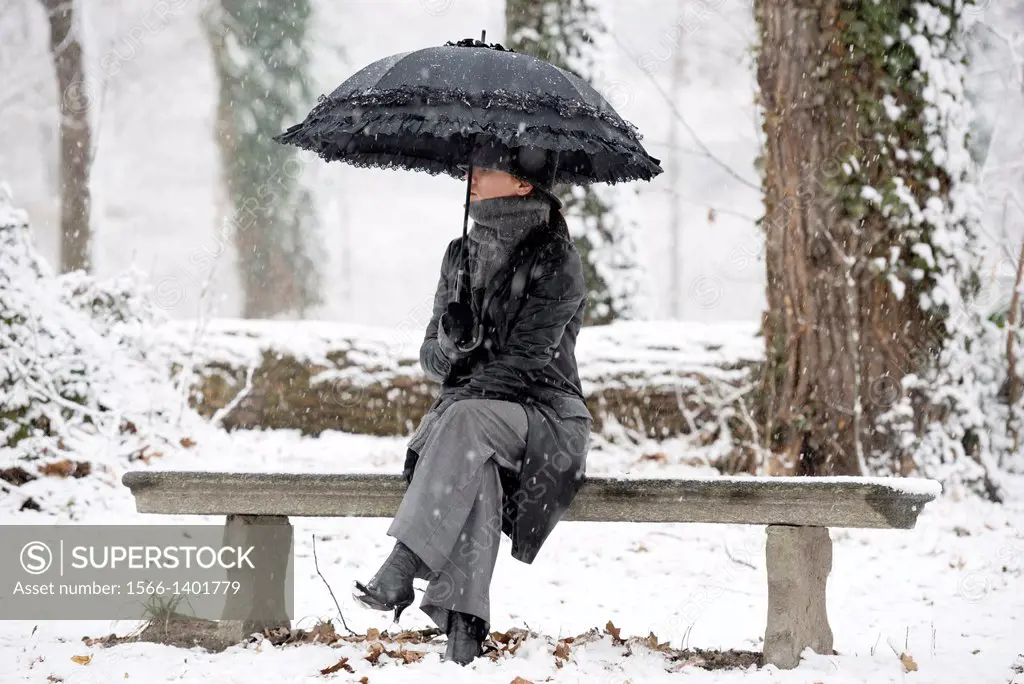 Elegant woman sitting on a bench with umbrella when it´s snowing in locarno ticino switzerland.