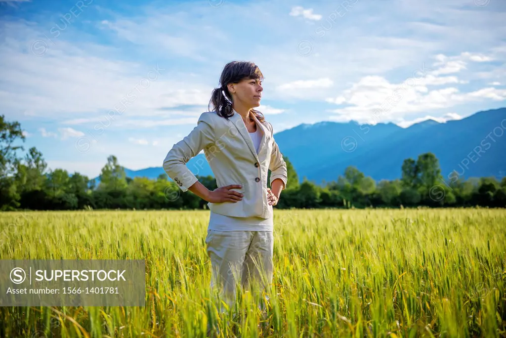 Proud woman standing up on a wheat field with mountain in background in ticino switzerland.