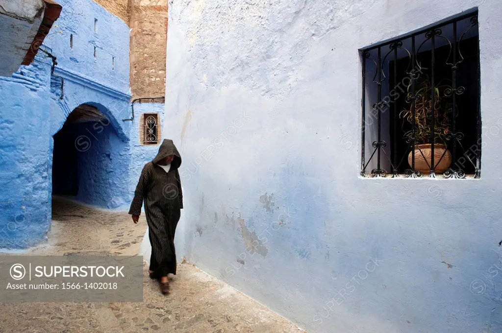Man dressed traditionally walking in a street in the Chefchaouen Old Town Medina, Morocco.