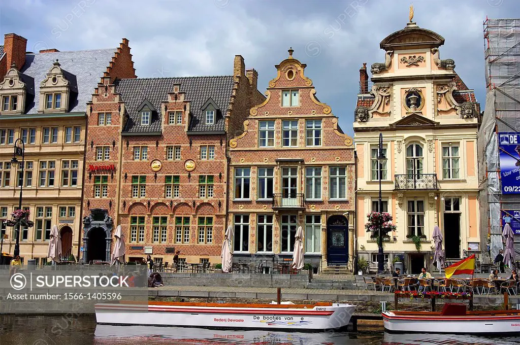 Schoolchildren and cafe patrons sit on a Ghent quay lined with historic architecture.
