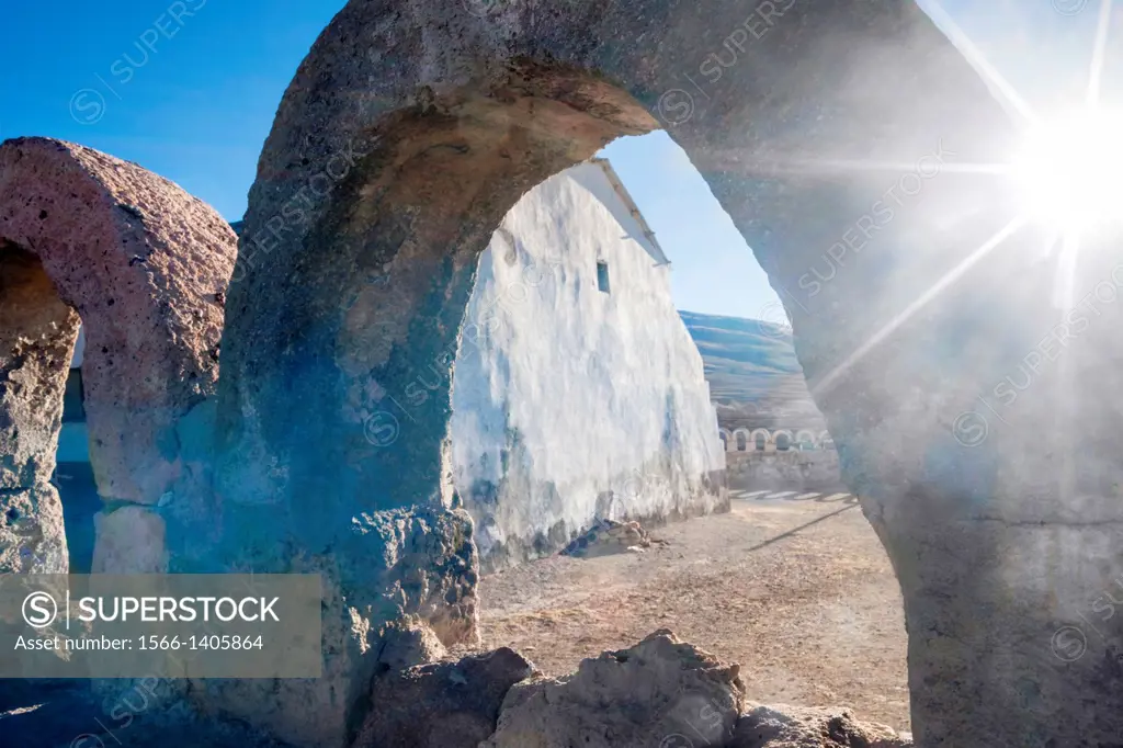 Backlit shot with sun star of limestone arch fence surrounding the remote church San Juan Bautista on edge of salt flats, Salar de Uyuni, Bolivia, Sou...
