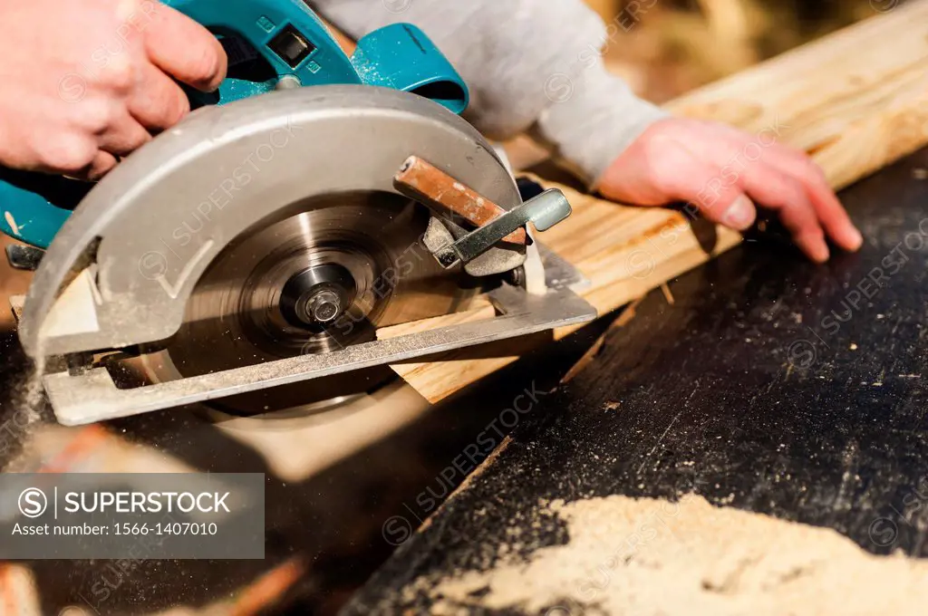 A man cuts a piece of lumber with a circular power saw.