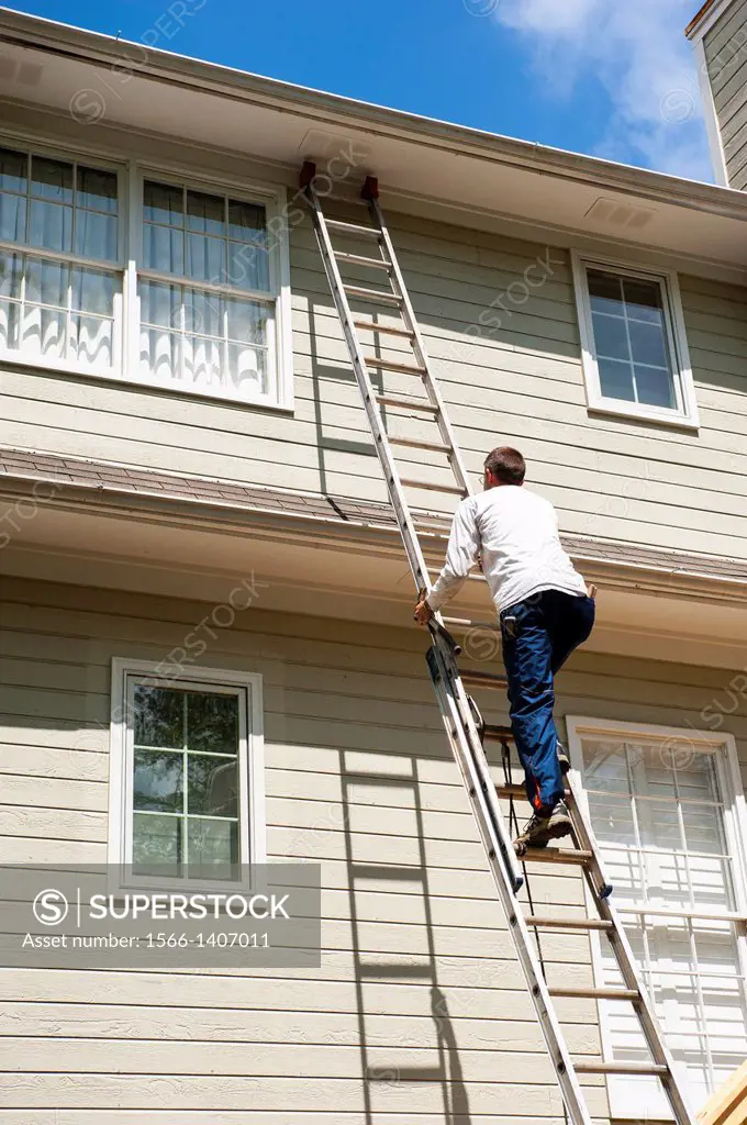 A man climbs a ladder up the side of a house.