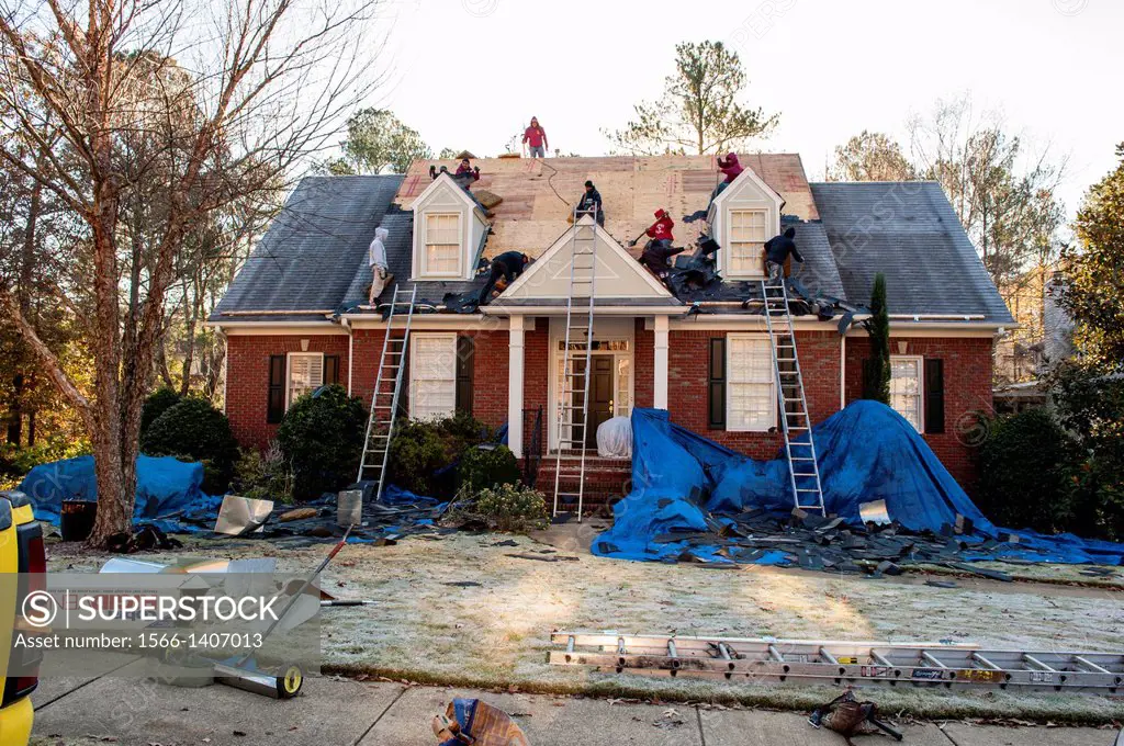 A roofing crew scrapes old shingles off of a house.