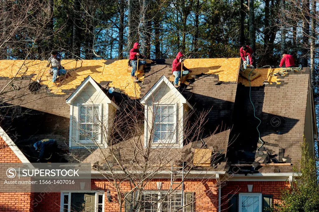 A roofing crew scrapes old shingles off of a house.