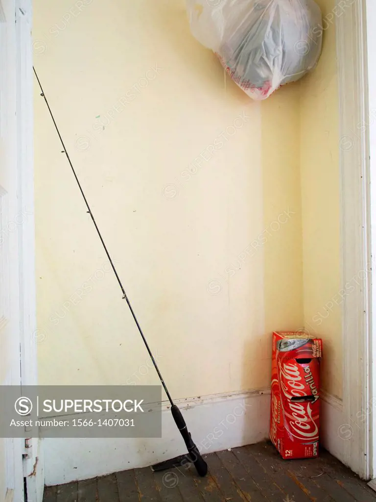 Fishing rod with coke package and plastic bag in corner of a room