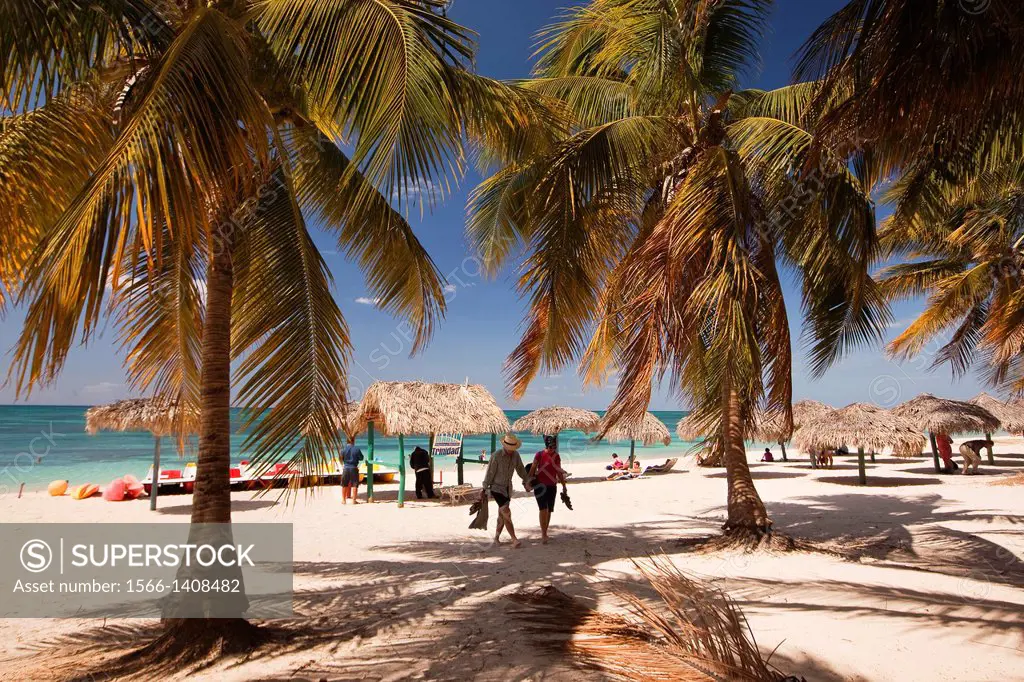 Tourists, parasols and thatched umbrellas on the beach of Playa Ancon near Trinidad, Sancti Spíritus, Cuba, West Indies, Central America.