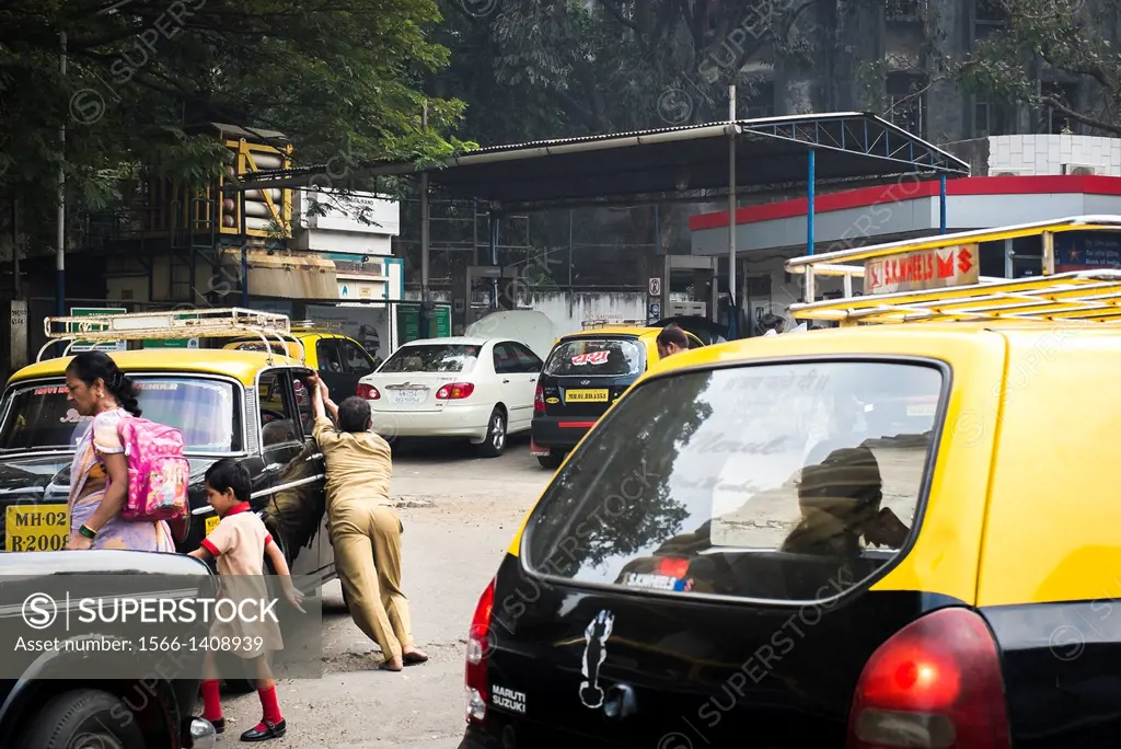 A taxi driver pushes his broken down taxi to a service station, while a woman walks a child back from school.
