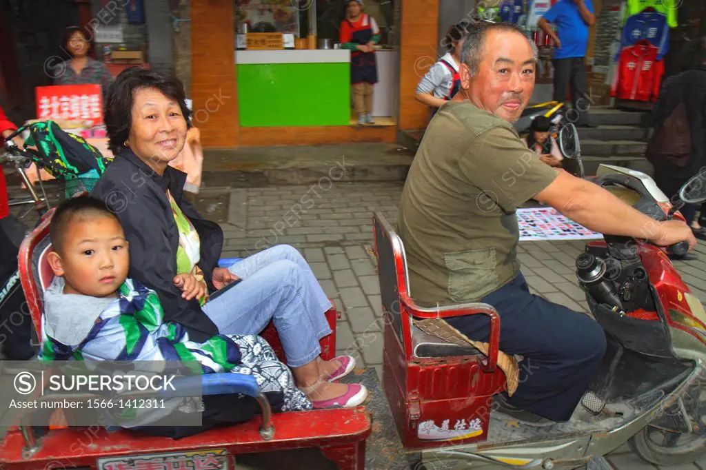 China, Beijing, Dongcheng District, Nanluoguxiang, hutong, historic, shopping, Asian, man, electric scooter cart, pedicab, passengers, woman, grandmot...