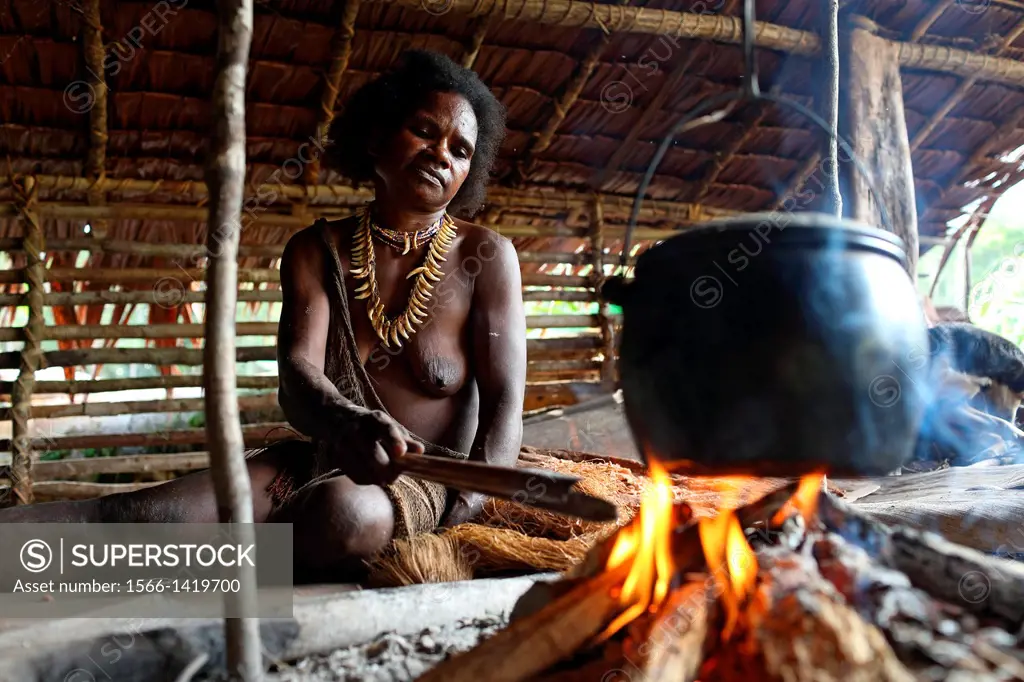 Kombai woman sitting with necklace made of dog teeth at the fire place and cooking, Papua, Indonesia, Southeast Asia.