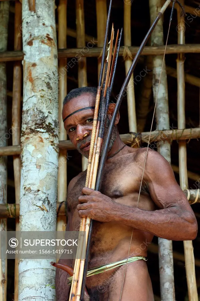 Kombai man standing in front of his wooden house with bow and arrows, Papua, Indonesia, Southeast Asia.