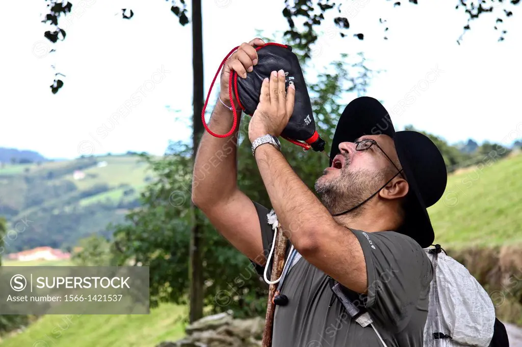 Pilgrim drinking wineskin at primitive way of Saint- Jacques, Asturias, Spain.