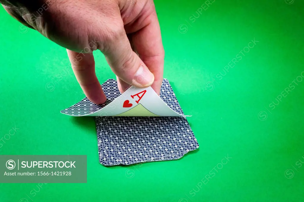 Hand discovering a lcard of poker as hearts on a green background.