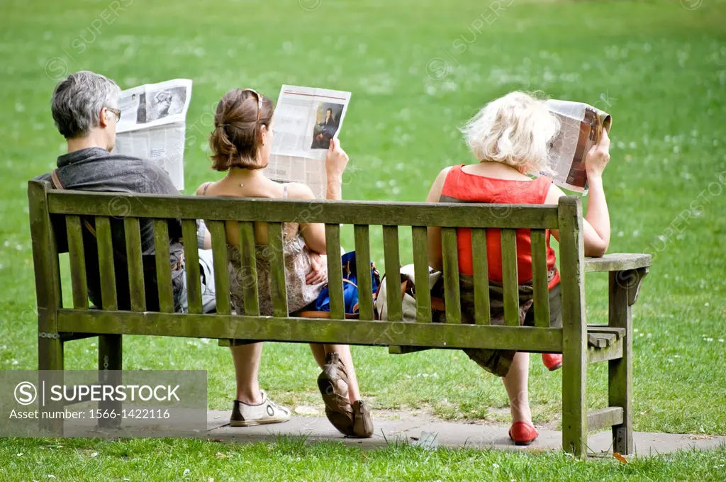 Three people on a garden bench read newspapers, taken in London on April 2011.