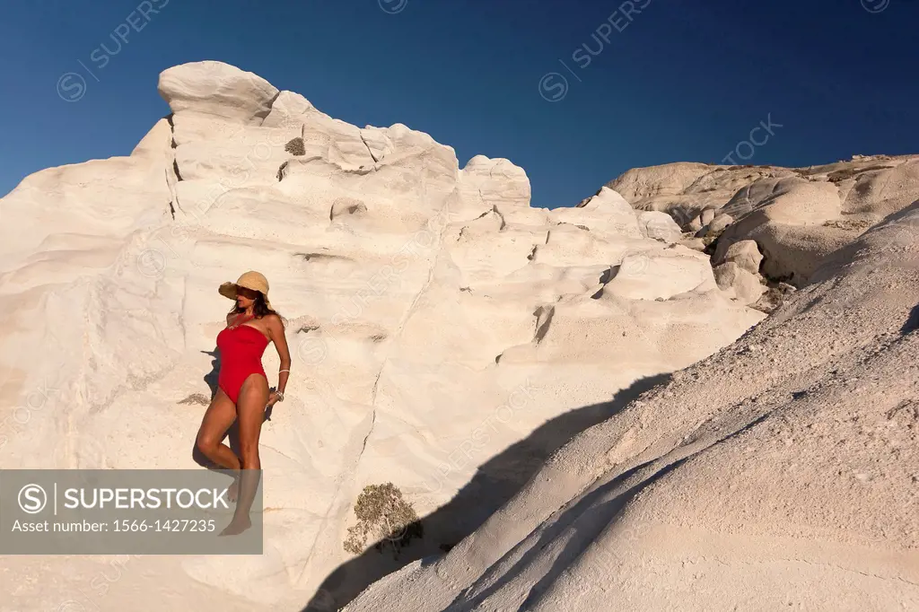 Woman with red swimsuit posing near the white rock forms in Sarakiniko beach, Milos, Cyclades Islands, Greek Islands, Greece, Europe.