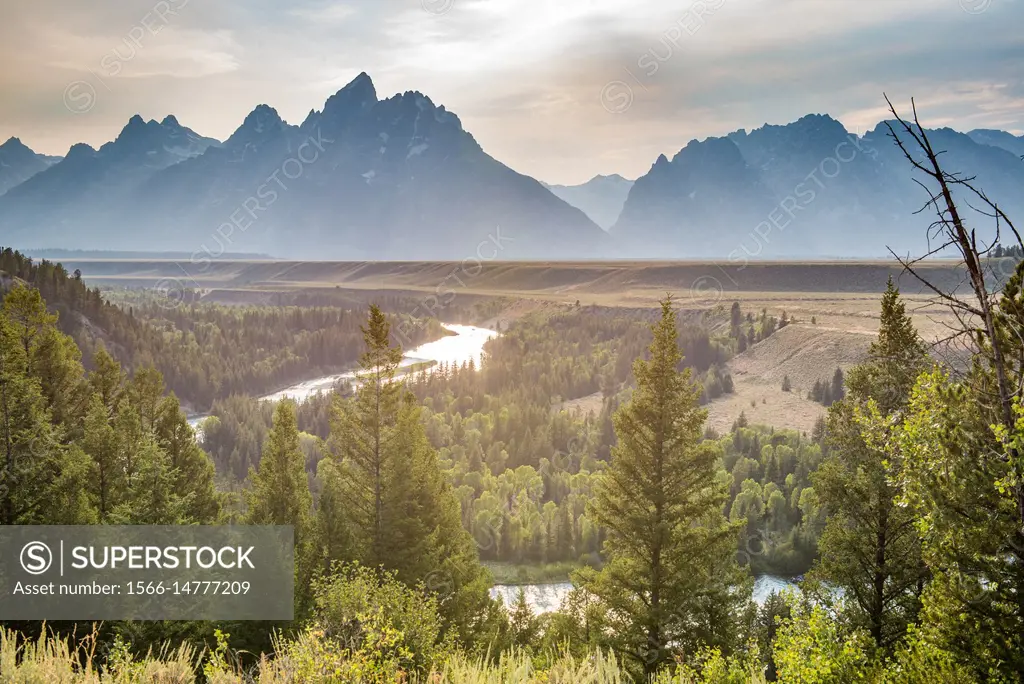 Snake River overlook shows Teton Mountain Range looming over illuminated forest and Snake River at dusk, Grand Tetons National Park, Teton County, Wyo...