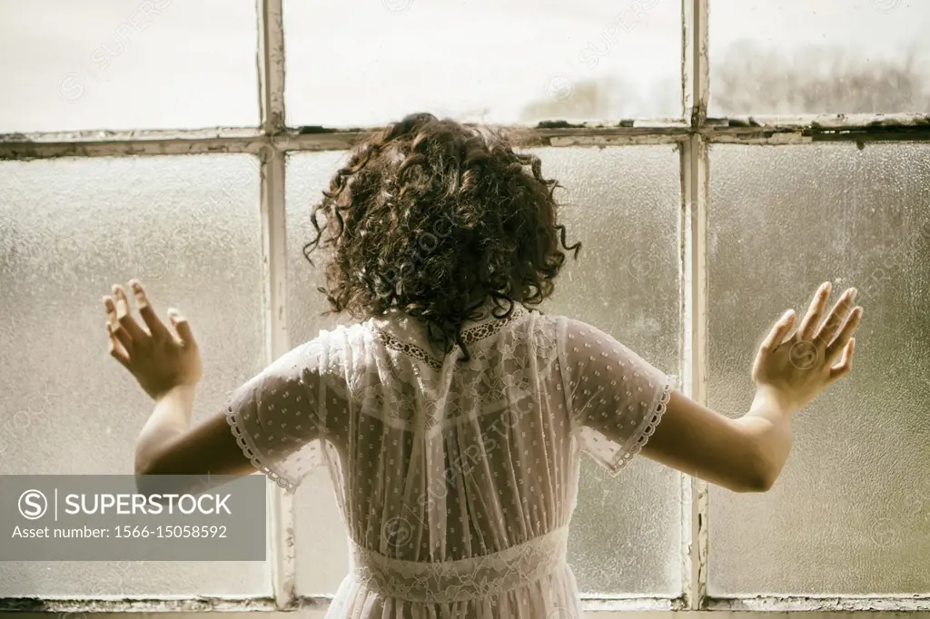 Rear view of a woman standing by the window hands touching the glass.
