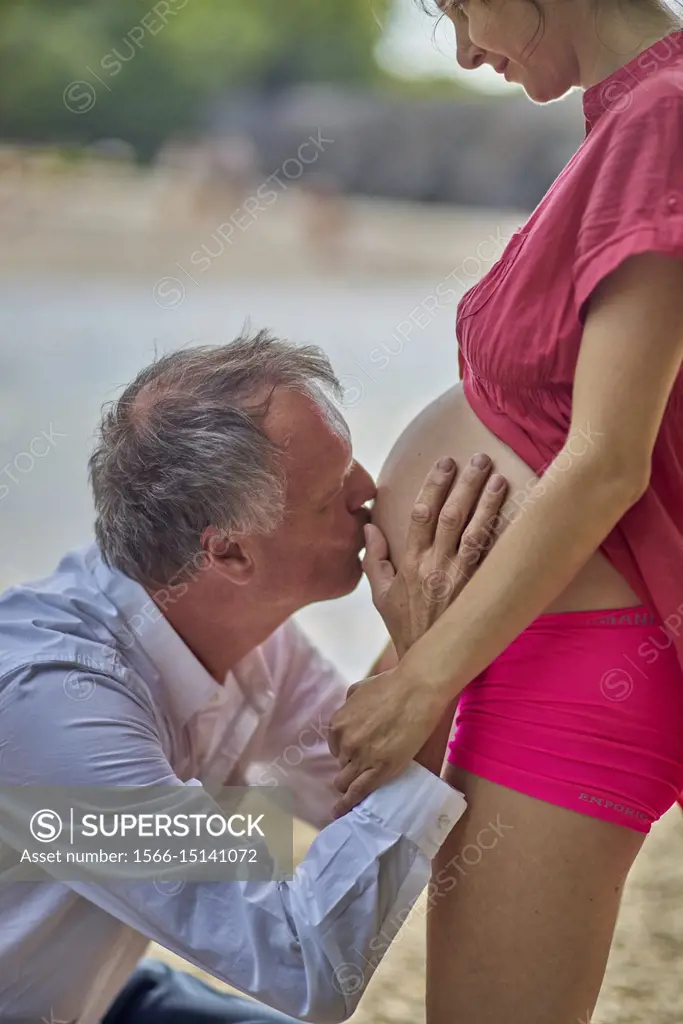 Man kissing pregnant woman on belly. At river Isar, Munich, Germany.