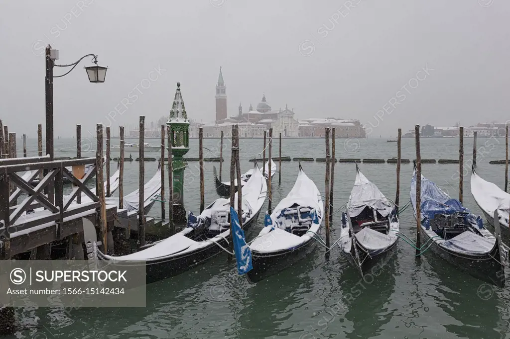 Some traditional venetian gondolas moored at Riva degli Schiavoni during a snowfall, Venice, Veneto, Italy.