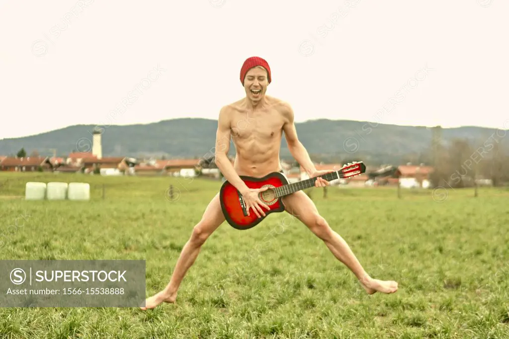naked young man jumping on countryside meadow with guitar, musician, rebel, naked, in Waakirchen, Bavaria, Germany