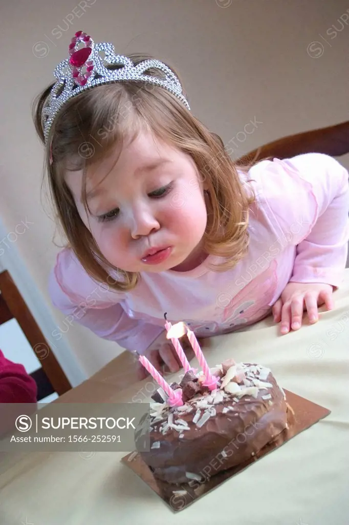 3 year old girl blowing a candle out on her birthday cake cake