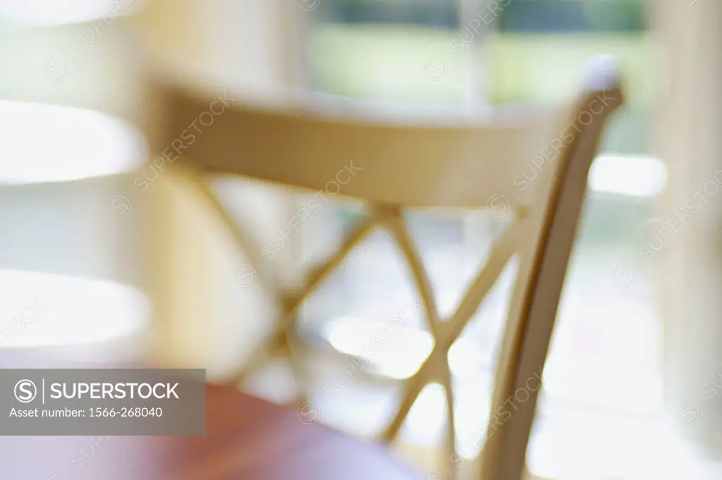 White wooden chair at wooden table, window behind in eating area, abstract view with selective focus and blur.