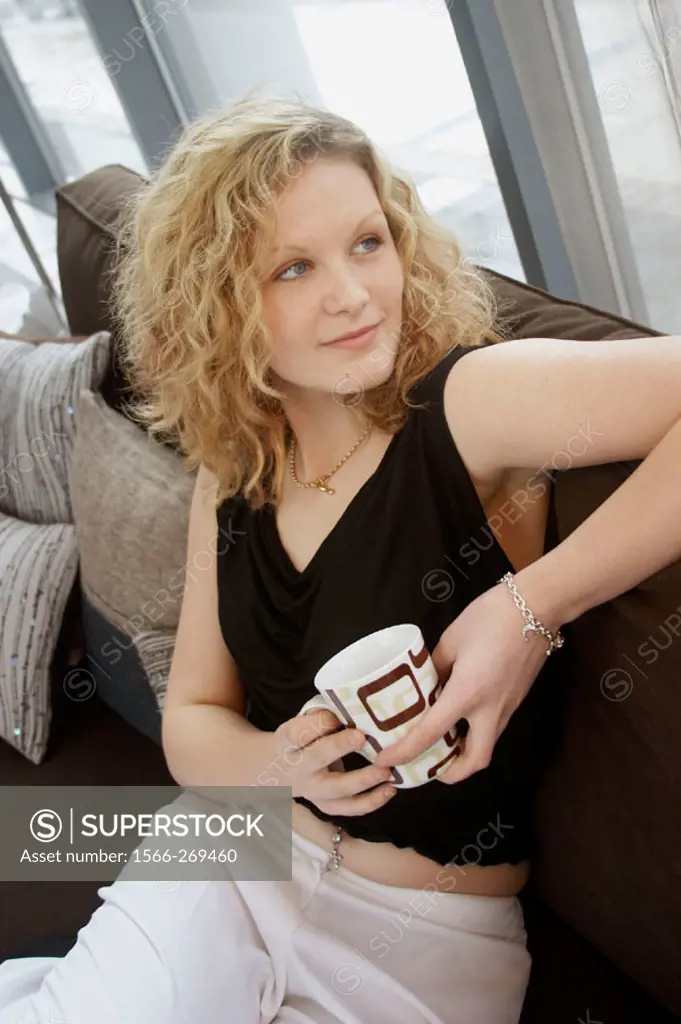 20 year old girl sitting on the sofa, with a coffee, smiling off camera