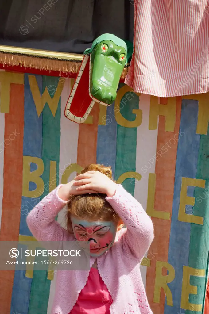3 year old girl standing in front of a Punch and Judy stall, with a crocodile snapping at her head.